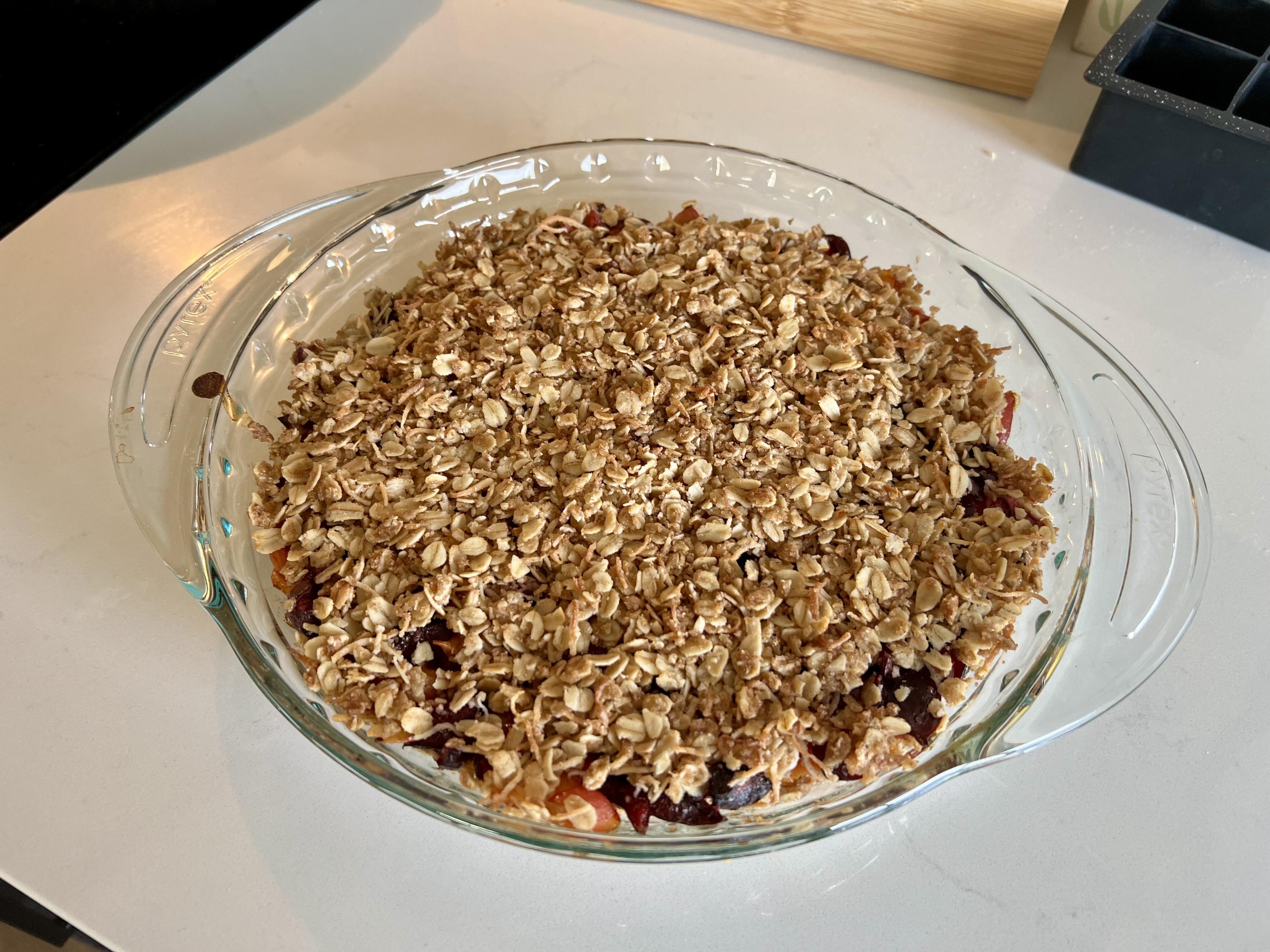 A top down view of a cherry crumble in a Pyrex dish. The top is covered in oats and some the of cherries are visible around the edges.