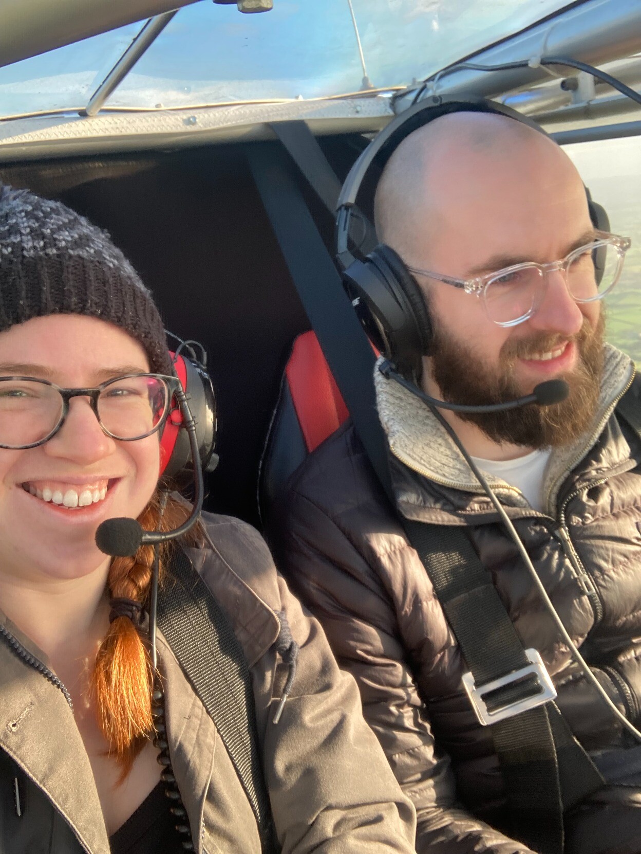 My wife Ellie and I in the cockpit of a light aircraft. Were both smiling and wearing aviation headsets.