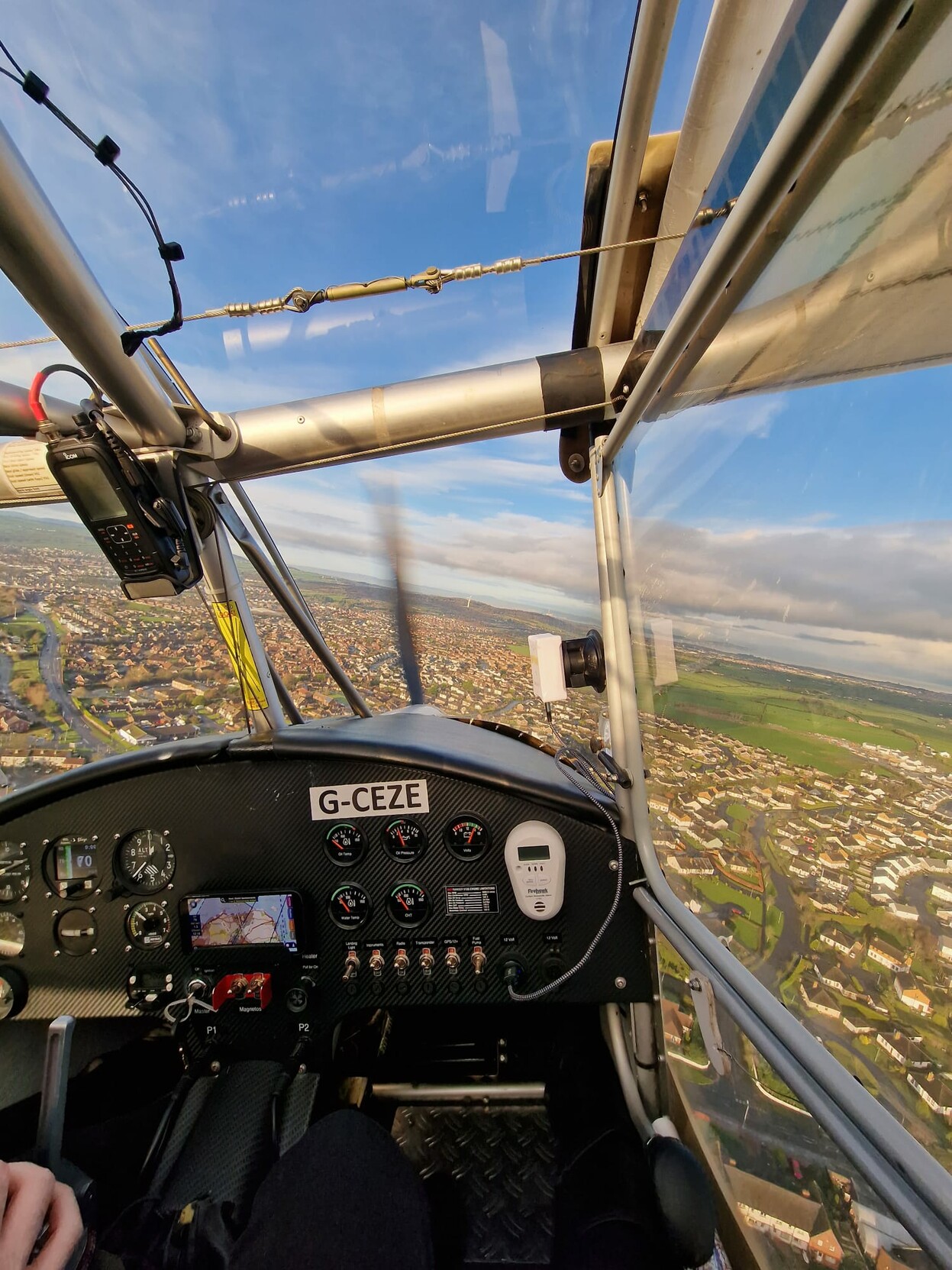 The passengers view from the cockpit of a light aircraft. Switches and dials are visible on the dashboard. Outside of the plane you can see the town ( Newtownards) below.